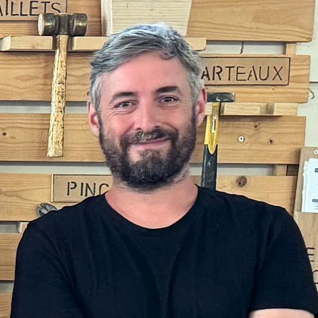 François, souriant devant le panneau des maillets et marteaux.